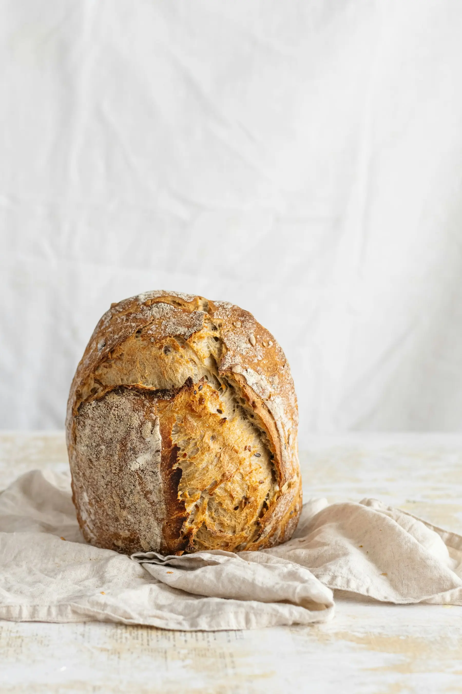 A seeded sourdough loaf, still dusted with flour, on a linen cloth.